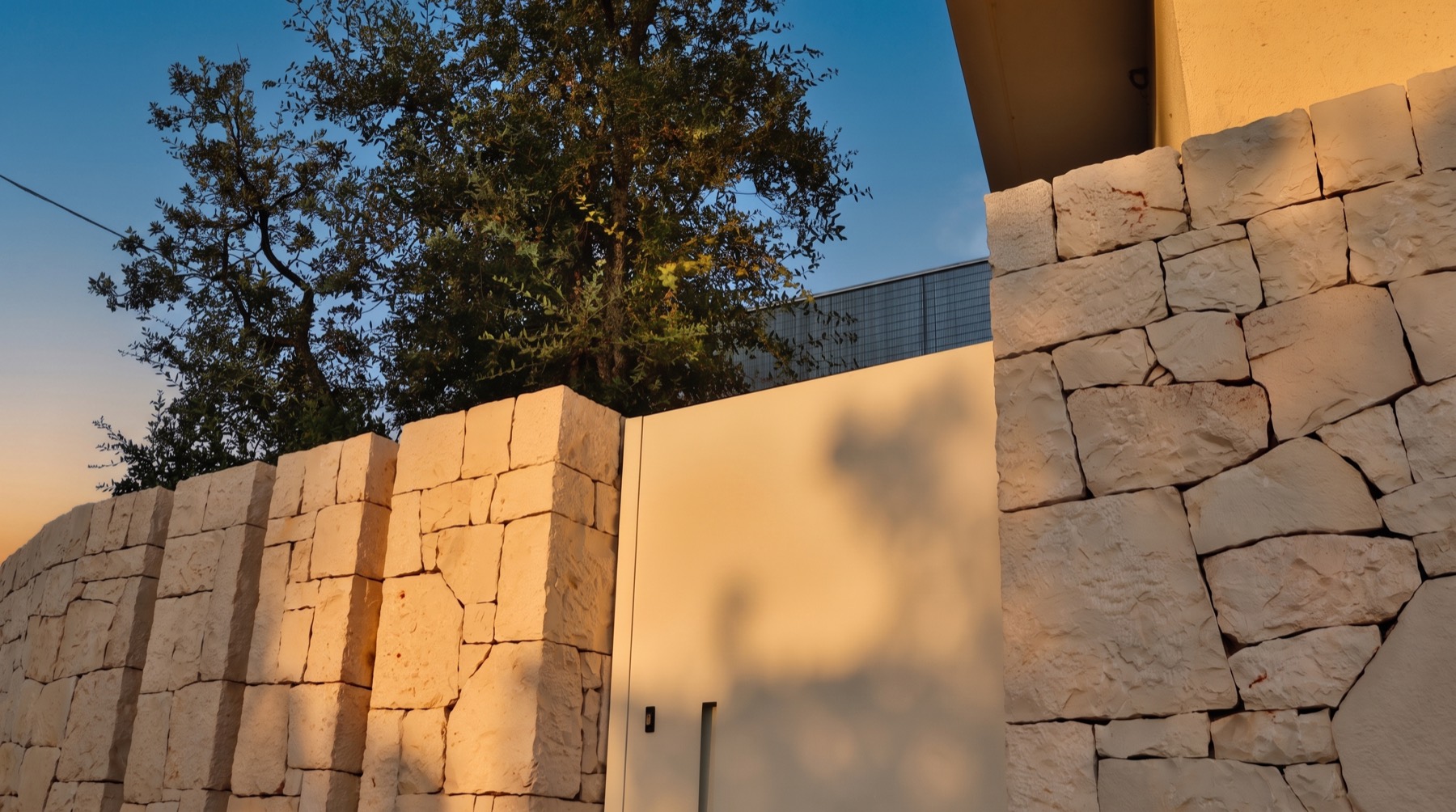 Il muro in pietra dell&rsquo;ingresso con l&rsquo;albero alle spalle al tramonto